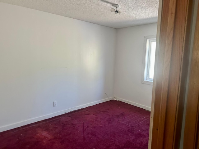unfurnished room featuring dark carpet, baseboards, and a textured ceiling
