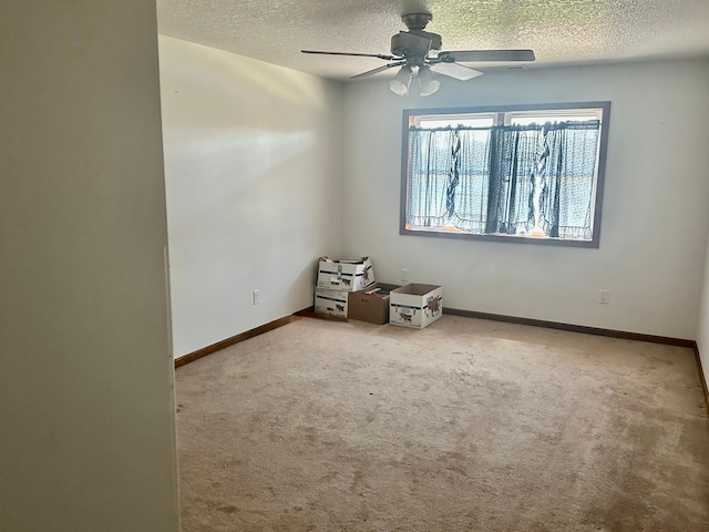 carpeted spare room featuring a textured ceiling, ceiling fan, and baseboards