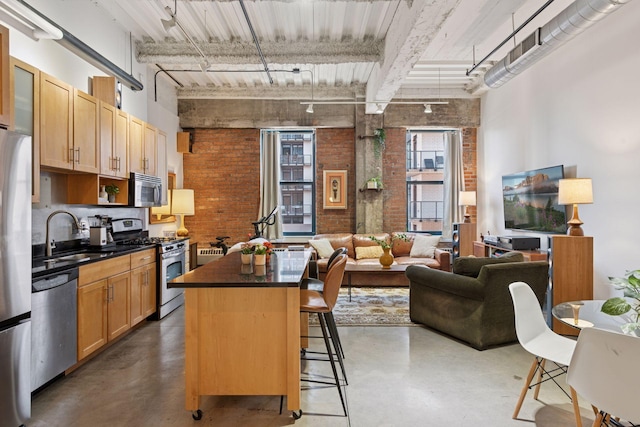 kitchen featuring brick wall, appliances with stainless steel finishes, a sink, finished concrete floors, and dark countertops