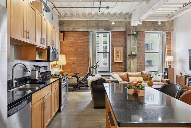 kitchen with stainless steel appliances, a sink, brick wall, finished concrete floors, and rail lighting