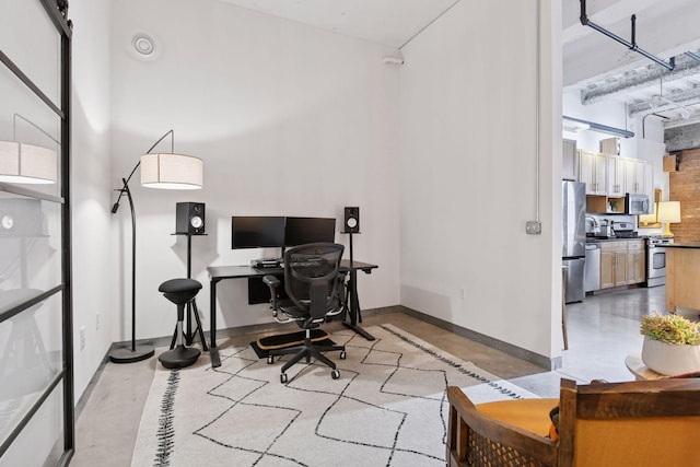 office area with concrete flooring, baseboards, a high ceiling, and a sink