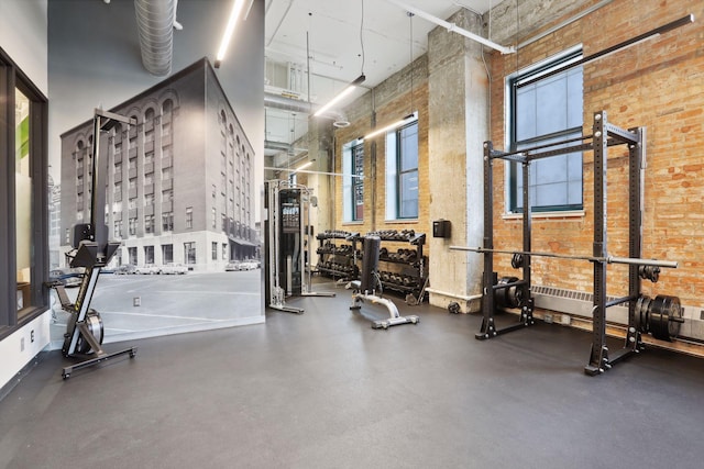 exercise room featuring a towering ceiling, healthy amount of natural light, and brick wall