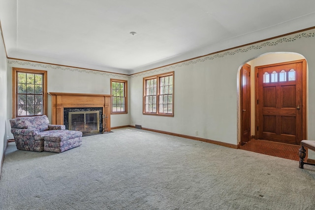 unfurnished living room featuring carpet, arched walkways, healthy amount of natural light, a premium fireplace, and crown molding