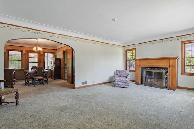 carpeted living area featuring arched walkways, a chandelier, baseboards, a high end fireplace, and ornamental molding