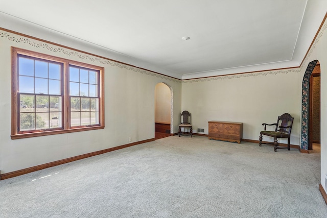unfurnished room featuring arched walkways, carpet floors, baseboards, and crown molding