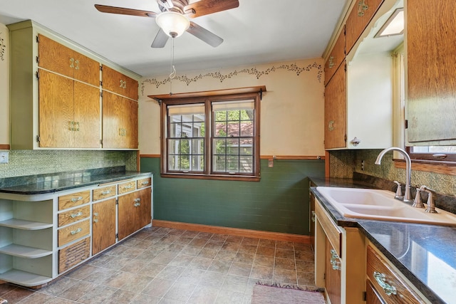 kitchen with a sink, a ceiling fan, baseboards, dark countertops, and a wainscoted wall