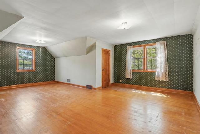 bonus room featuring wallpapered walls, wood finished floors, baseboards, and lofted ceiling