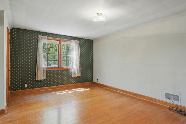 empty room featuring wallpapered walls, baseboards, wood finished floors, and vaulted ceiling
