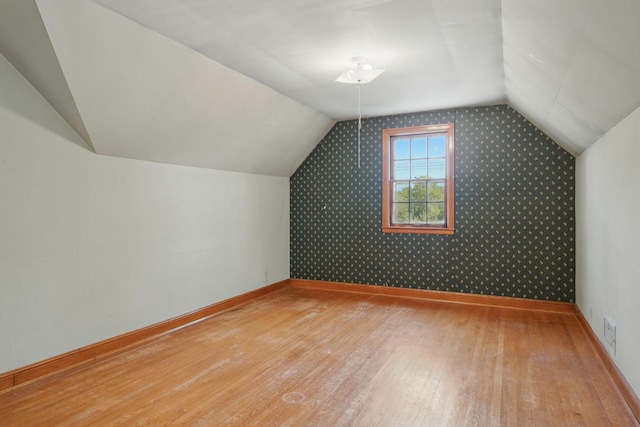 additional living space featuring wood finished floors, baseboards, lofted ceiling, and wallpapered walls