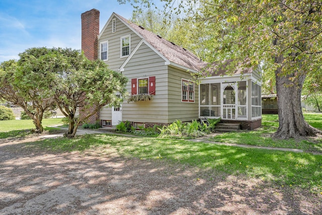 view of front facade with a sunroom, a chimney, entry steps, and a front yard