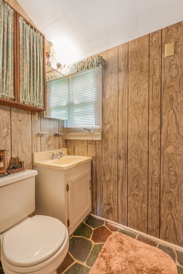 half bathroom featuring wooden walls, toilet, and vanity