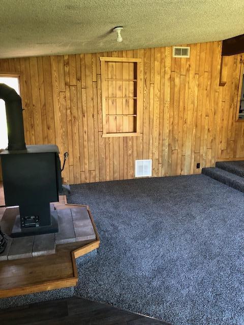 carpeted living room with a wood stove, wood walls, stairway, and a textured ceiling