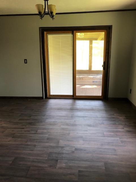 spare room featuring dark wood-style flooring, a chandelier, and baseboards