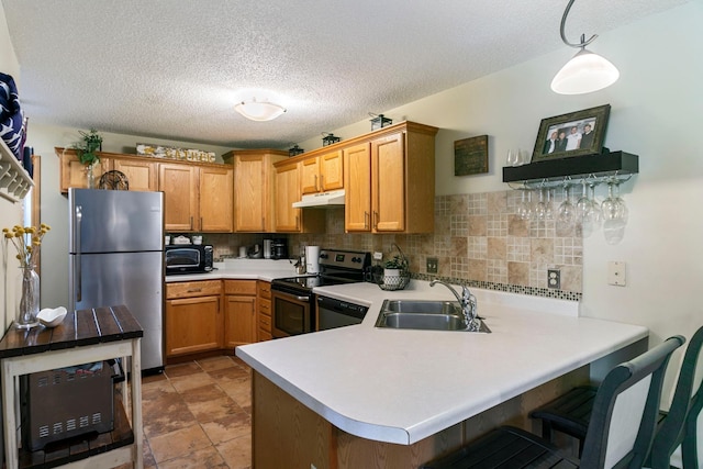 kitchen featuring appliances with stainless steel finishes, a sink, under cabinet range hood, light countertops, and a peninsula