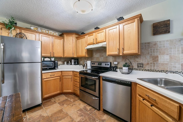 kitchen with stainless steel appliances, under cabinet range hood, light countertops, a sink, and a textured ceiling