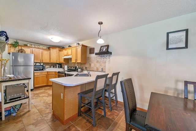 kitchen featuring appliances with stainless steel finishes, a peninsula, a textured ceiling, light countertops, and a breakfast bar