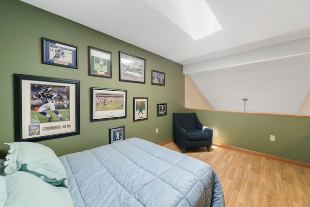 bedroom with wood finished floors, lofted ceiling, baseboards, and a skylight