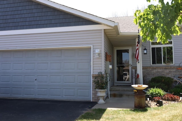 302 Pine St, Cannon Falls, MN 55009 - view of exterior entry with driveway, a garage, a shingled roof, and brick siding