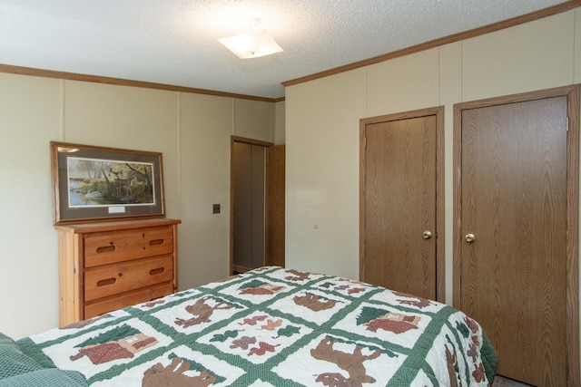 bedroom featuring crown molding, two closets, a decorative wall, and a textured ceiling
