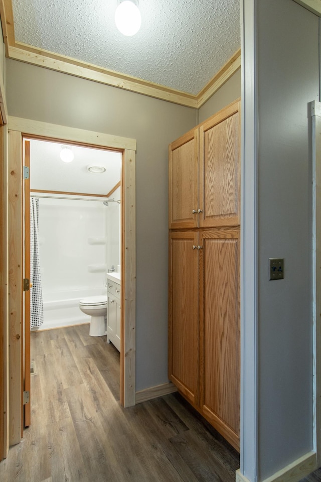 hallway featuring wood finished floors, a textured ceiling, and crown molding