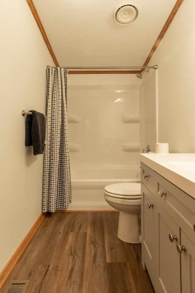 bathroom featuring toilet, wood finished floors, shower / bath combination with curtain, vanity, and a textured ceiling