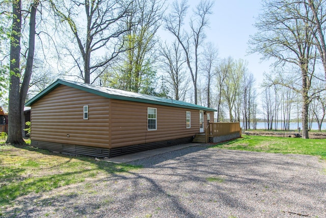 view of property exterior with log veneer siding, a deck with water view, and gravel driveway