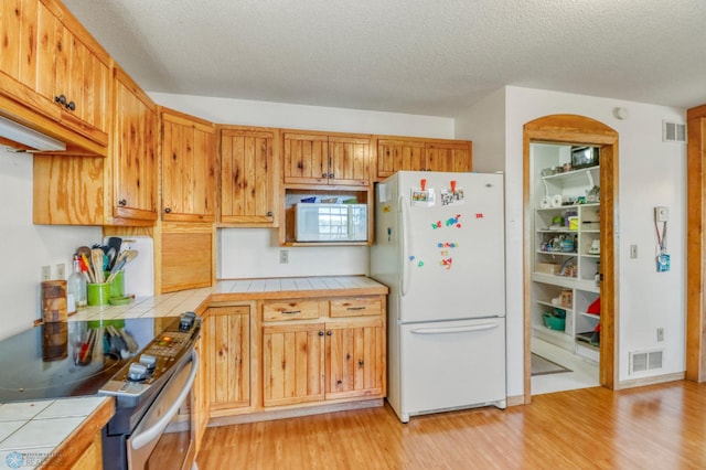 kitchen featuring white appliances, tile counters, light wood-type flooring, and a textured ceiling