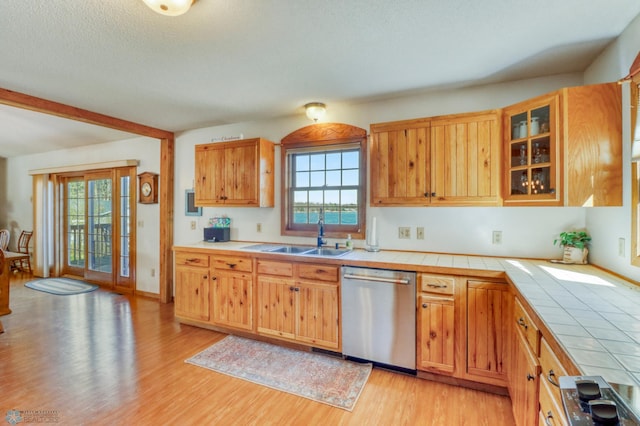 kitchen with stainless steel dishwasher, tile counters, a sink, plenty of natural light, and a textured ceiling