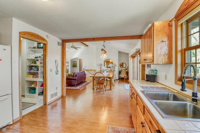 kitchen with tile countertops, a sink, freestanding refrigerator, light wood-style flooring, and a textured ceiling