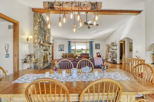 dining room featuring a fireplace, arched walkways, beam ceiling, wood finished floors, and high vaulted ceiling