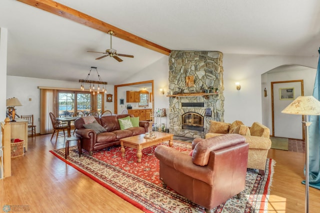 living area featuring a ceiling fan, wood finished floors, a stone fireplace, and arched walkways