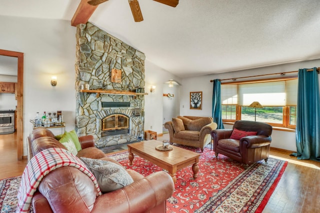 living area with wood finished floors, ceiling fan, a stone fireplace, and a textured ceiling