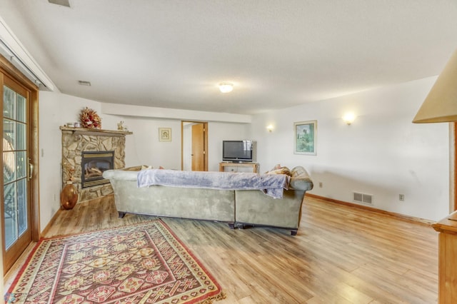living area with light wood finished floors, a stone fireplace, and baseboards