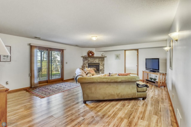 living room with light wood-style flooring, a stone fireplace, and baseboards