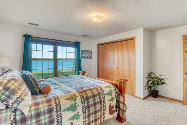 bedroom featuring carpet floors, a textured ceiling, a water view, a closet, and baseboards