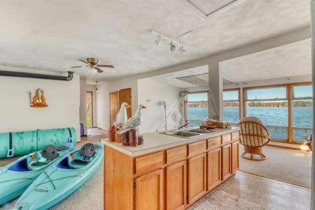 kitchen featuring a sink, track lighting, a water view, light countertops, and a ceiling fan