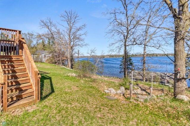 view of grassy yard with stairway and a deck with water view