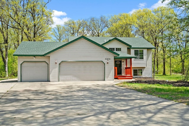 tri-level home featuring a garage, driveway, and roof with shingles