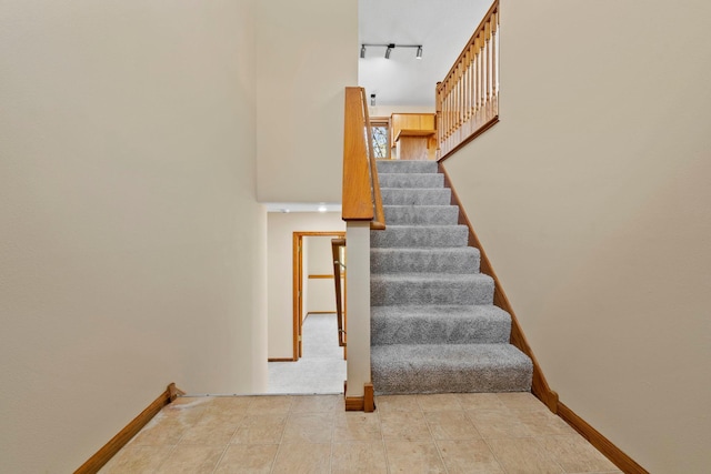 stairway with baseboards, rail lighting, and a high ceiling