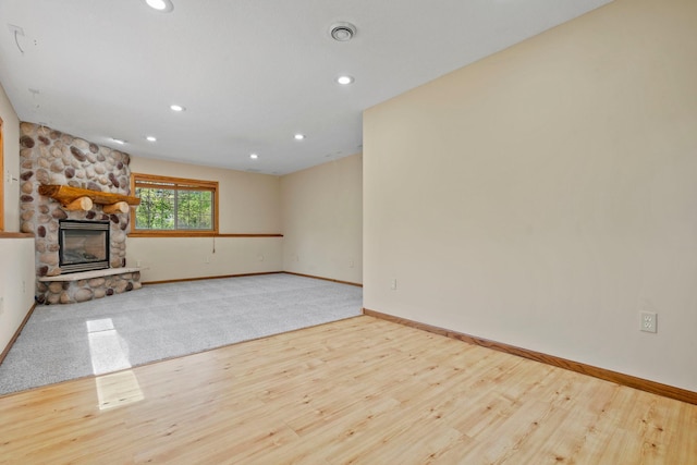 unfurnished living room featuring a stone fireplace, recessed lighting, wood finished floors, and baseboards