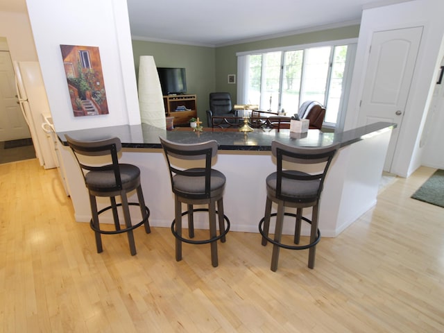 kitchen with light wood-style flooring, crown molding, dark countertops, and a kitchen bar