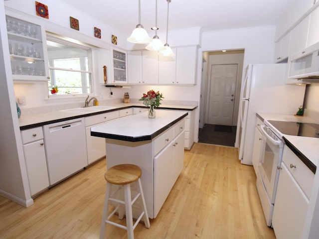 kitchen with white appliances, a sink, a center island, light wood finished floors, and white cabinets