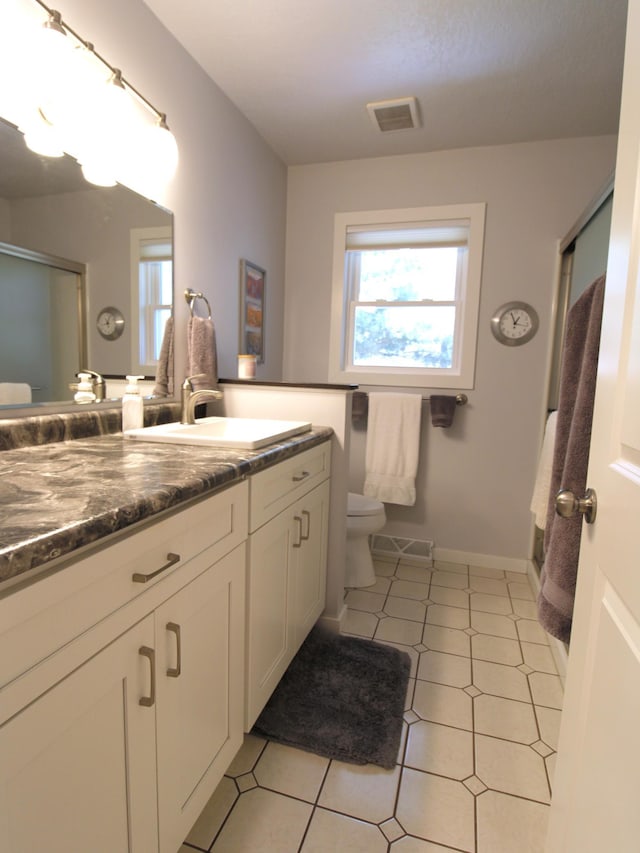 bathroom featuring toilet, a shower with door, vanity, and baseboards