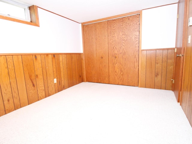 empty room featuring wooden walls, carpet flooring, and wainscoting