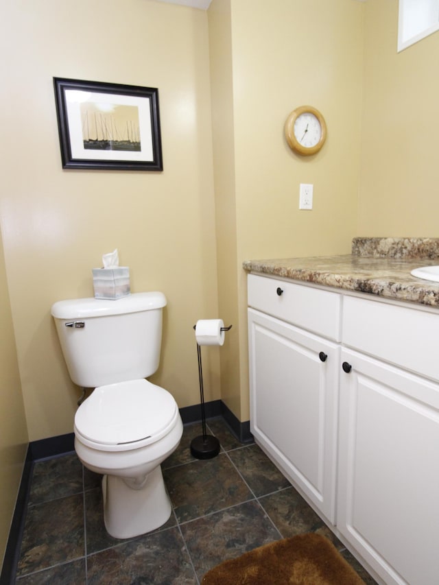 bathroom featuring baseboards, toilet, vanity, and stone finish flooring