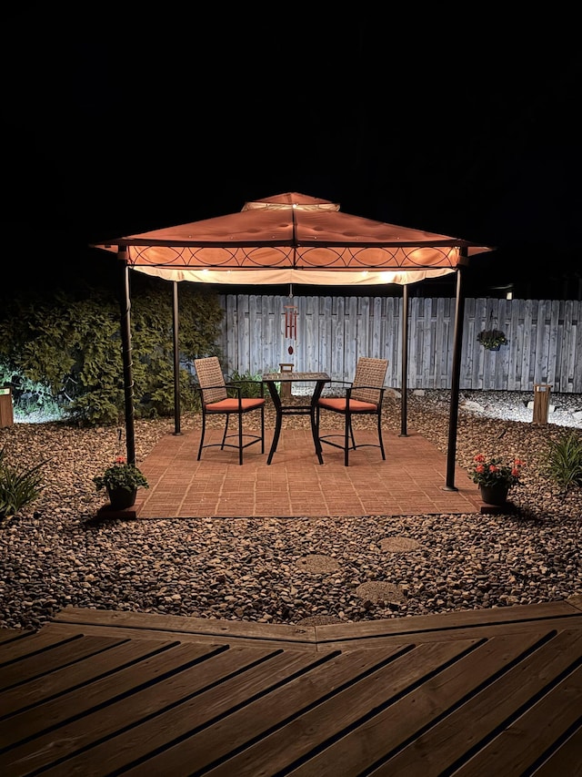 deck at twilight with a gazebo, fence, outdoor dining space, and a patio