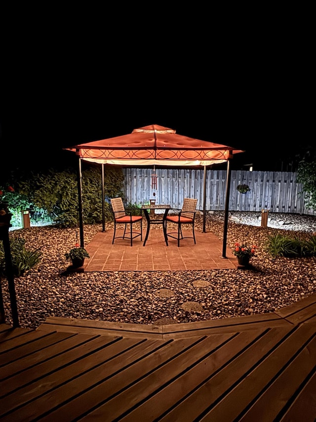 deck at night with a gazebo, fence, and a patio
