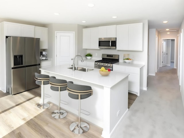 kitchen featuring appliances with stainless steel finishes, a sink, white cabinets, light countertops, and a kitchen breakfast bar