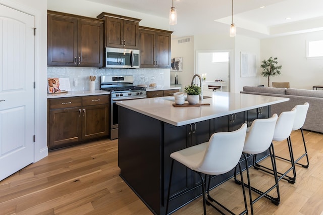 kitchen with appliances with stainless steel finishes, light wood finished floors, backsplash, a kitchen breakfast bar, and open floor plan