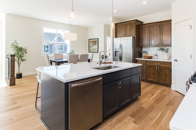 kitchen with stainless steel appliances, a sink, light countertops, light wood-style floors, and a kitchen island with sink